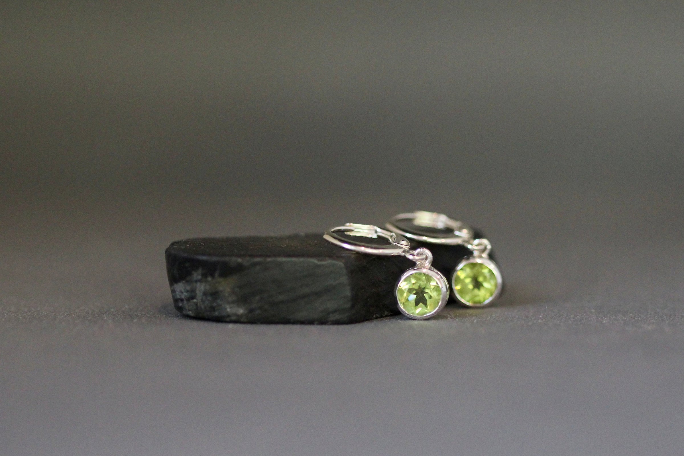 Silver huggie hoop earrings with two round green peridot bezel charms