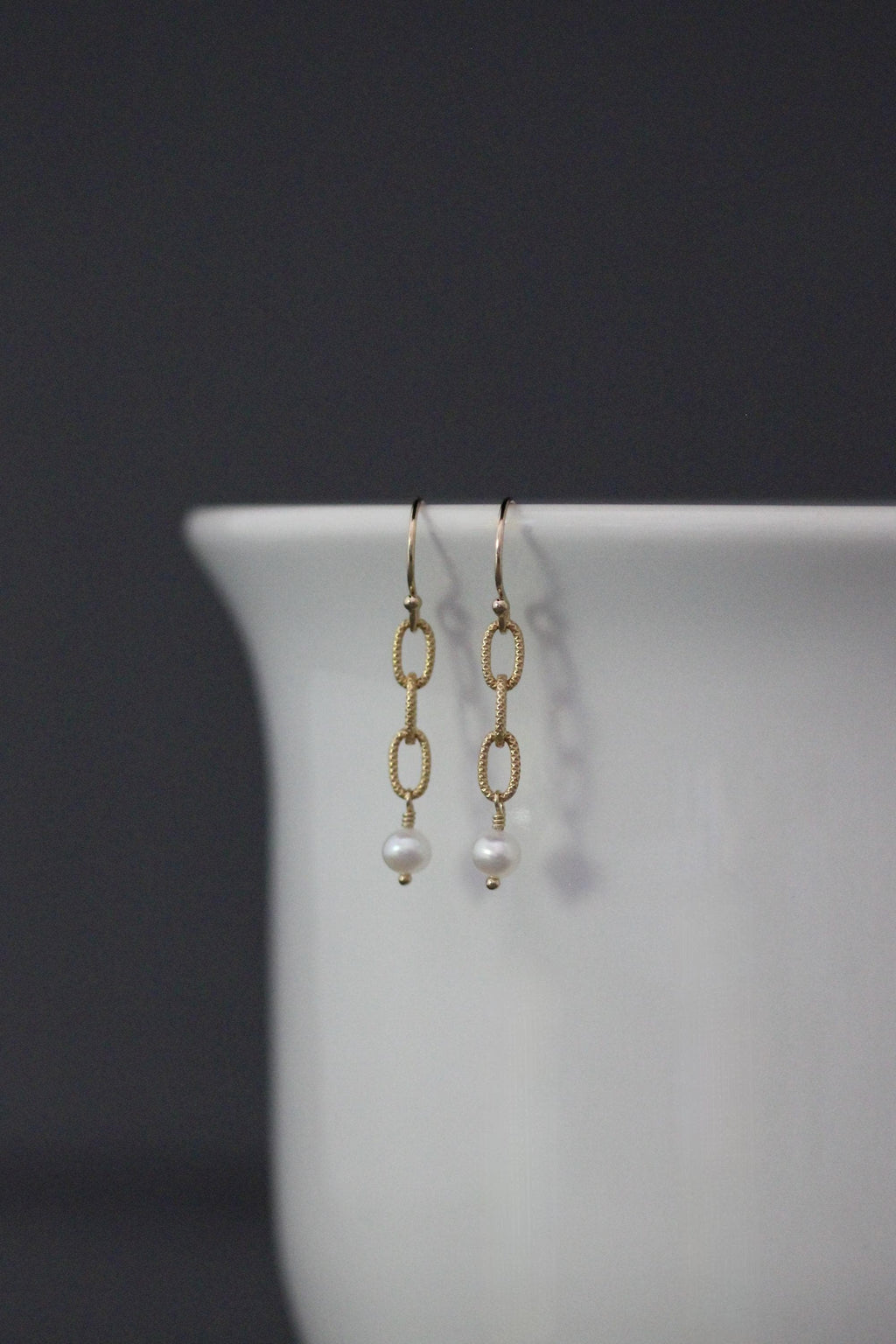 Gold drop earrings featuring chain links and a white freshwater pearl on each.