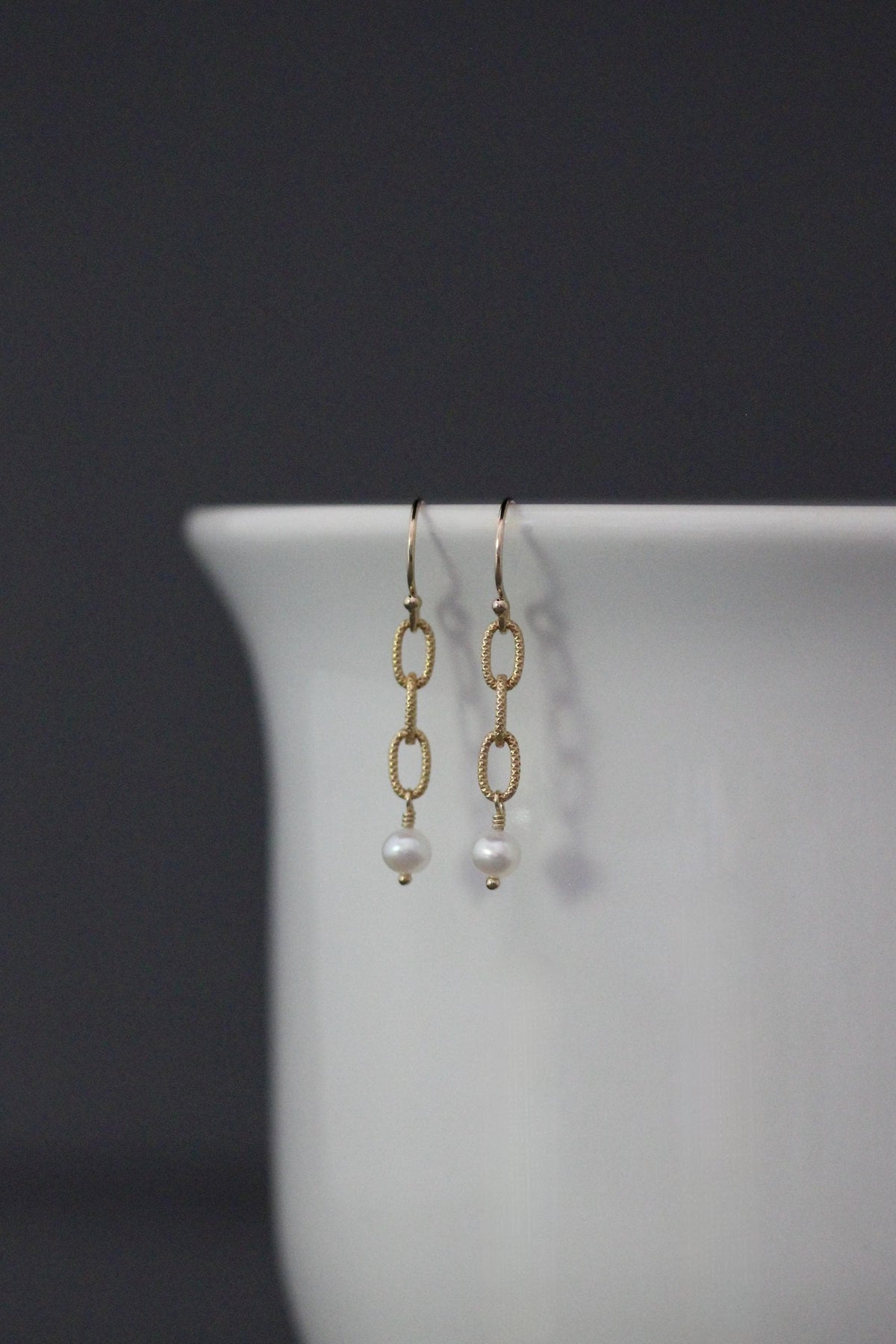 Gold drop earrings featuring chain links and a white freshwater pearl on each.