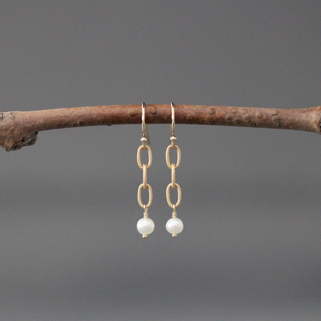 Gold chain-link dangle earrings with a white freshwater pearl at the bottom.