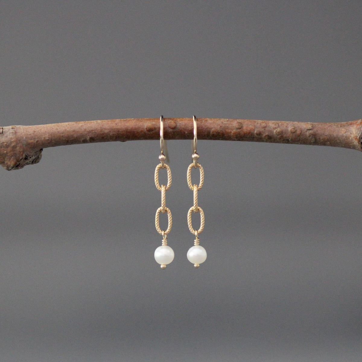 Gold chain-link dangle earrings with a white freshwater pearl at the bottom.