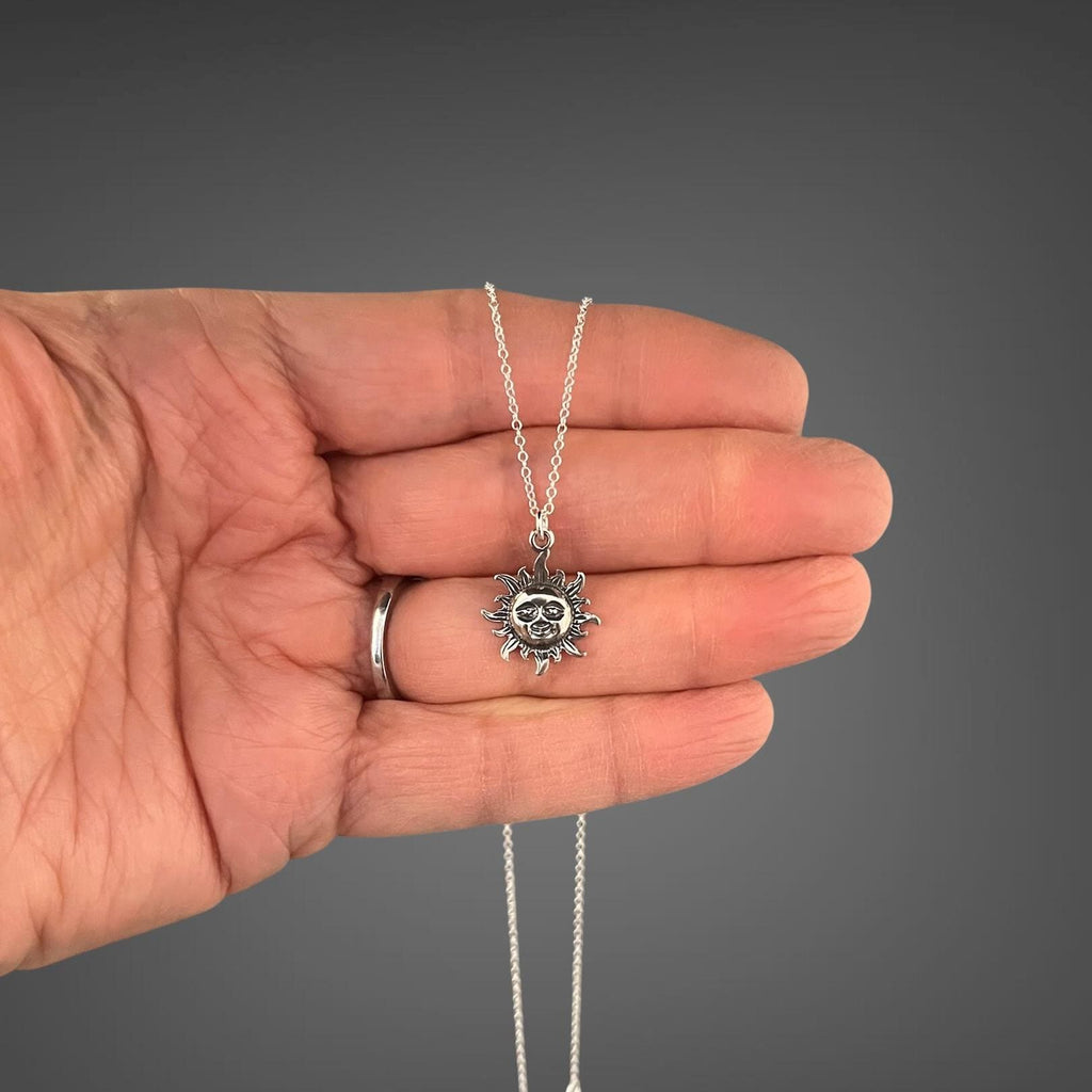 Sterling silver sun pendant necklace held in hand with small radiant sun charm