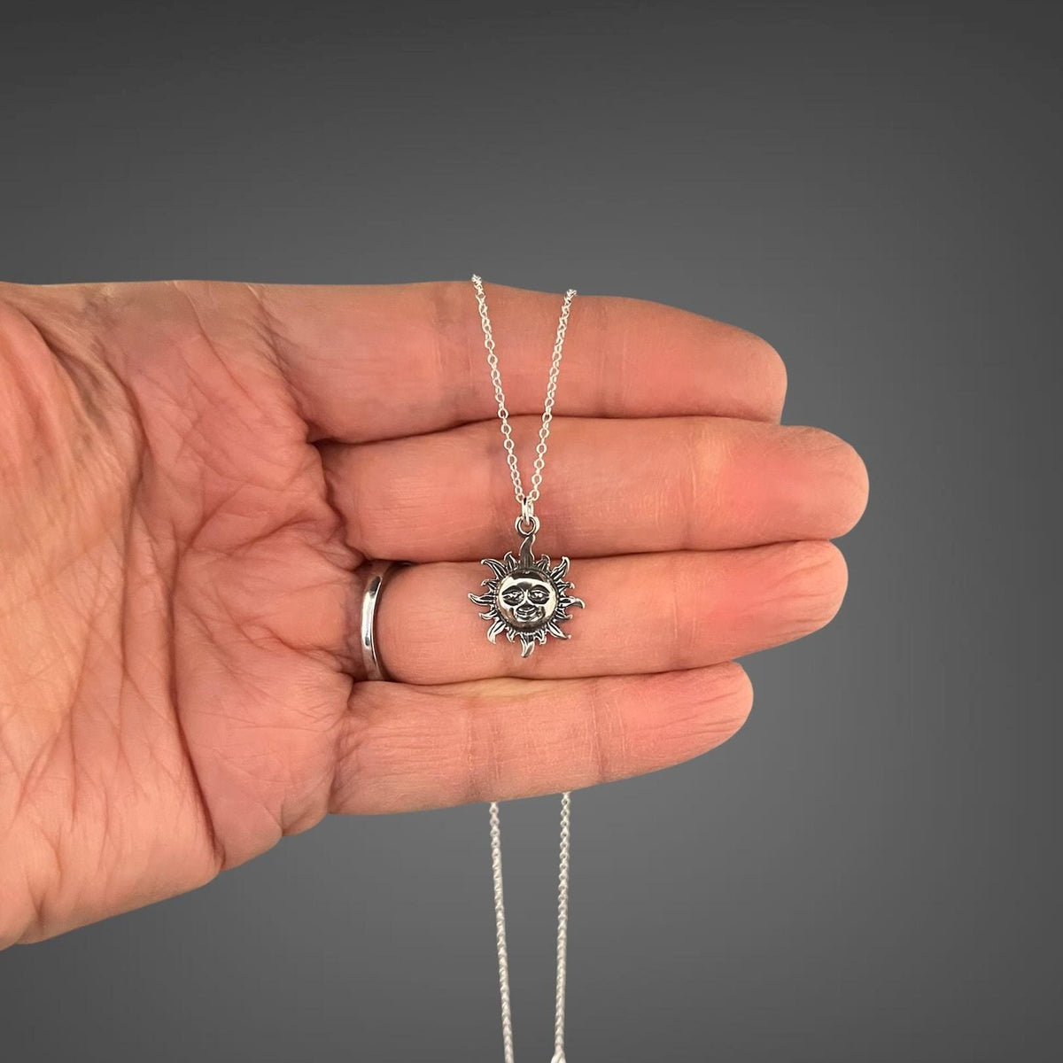 Sterling silver sun pendant necklace held in hand with small radiant sun charm