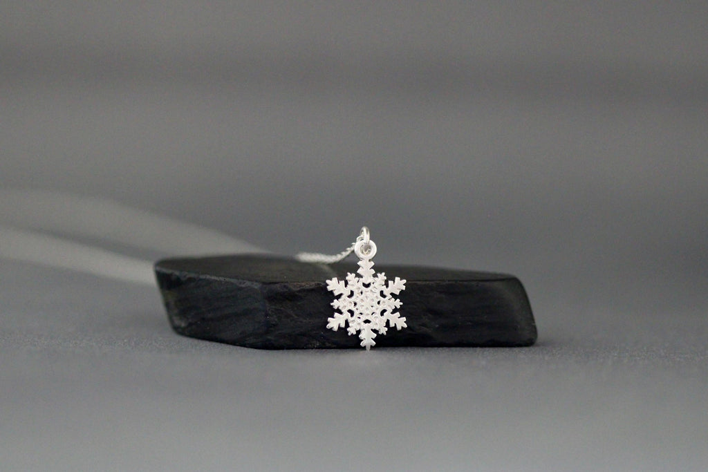 Sterling silver snowflake charm necklace lying flat with snowflake pendant centered