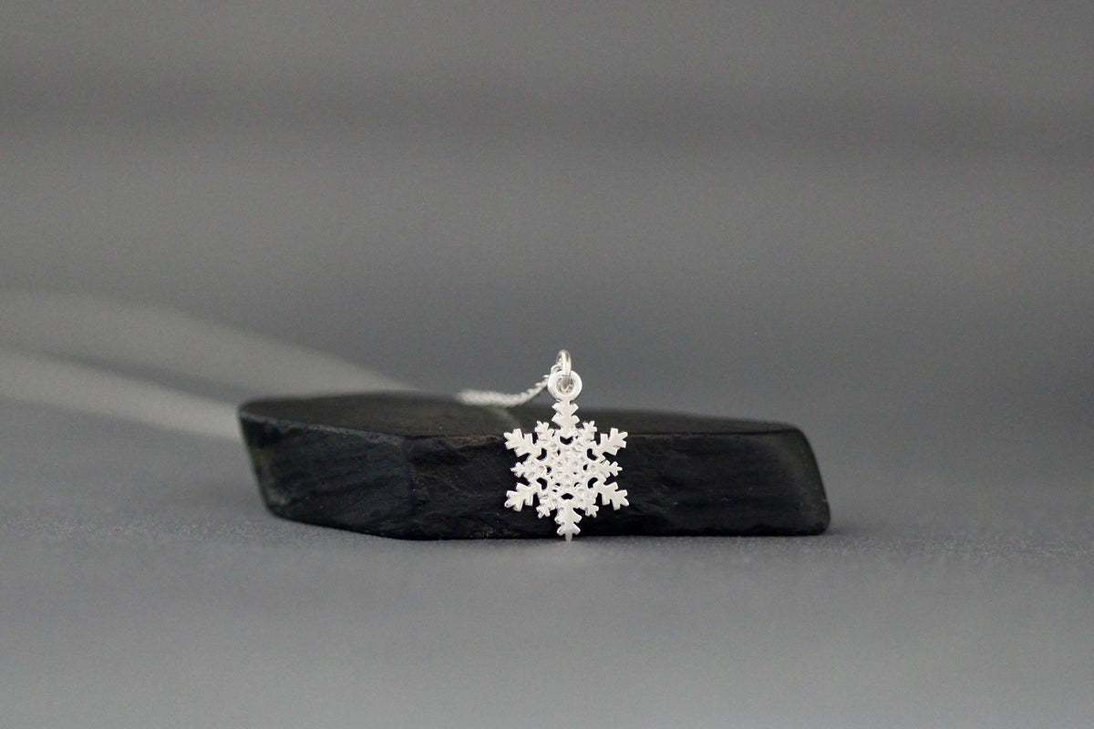 Sterling silver snowflake charm necklace lying flat with snowflake pendant centered