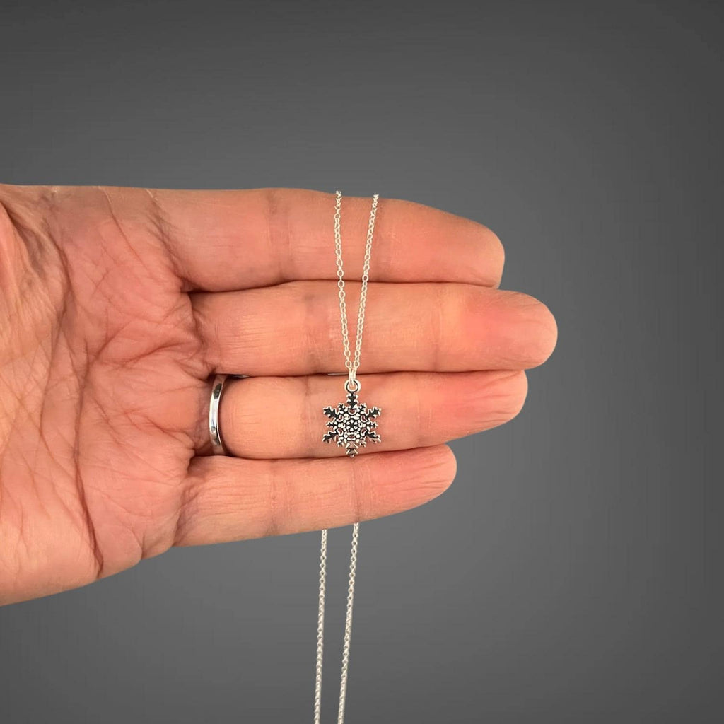 Sterling silver snowflake charm necklace held in hand with snowflake pendant close-up
