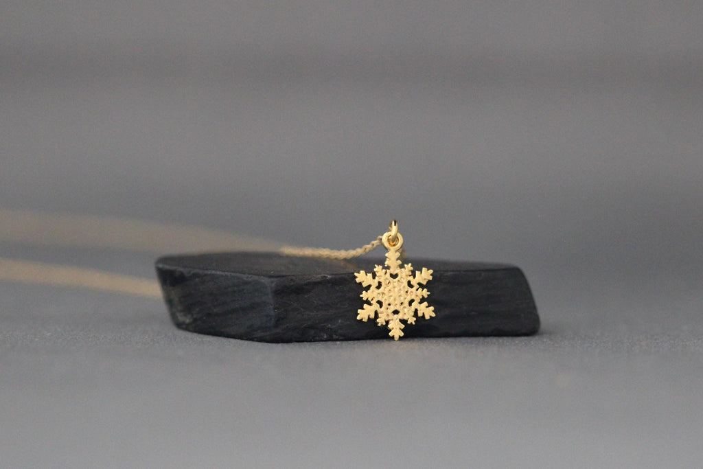 Gold snowflake charm pendant shown beside its fine chain