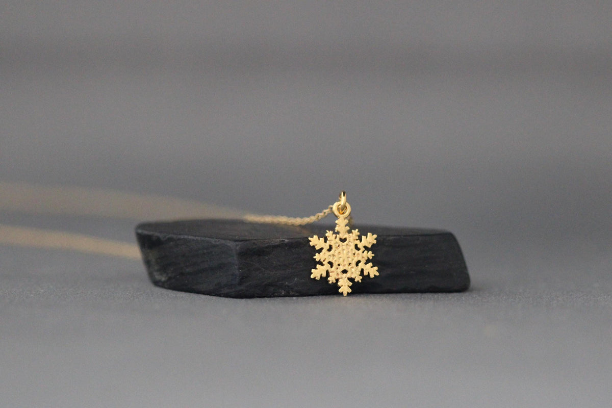 Gold snowflake charm pendant shown beside its fine chain