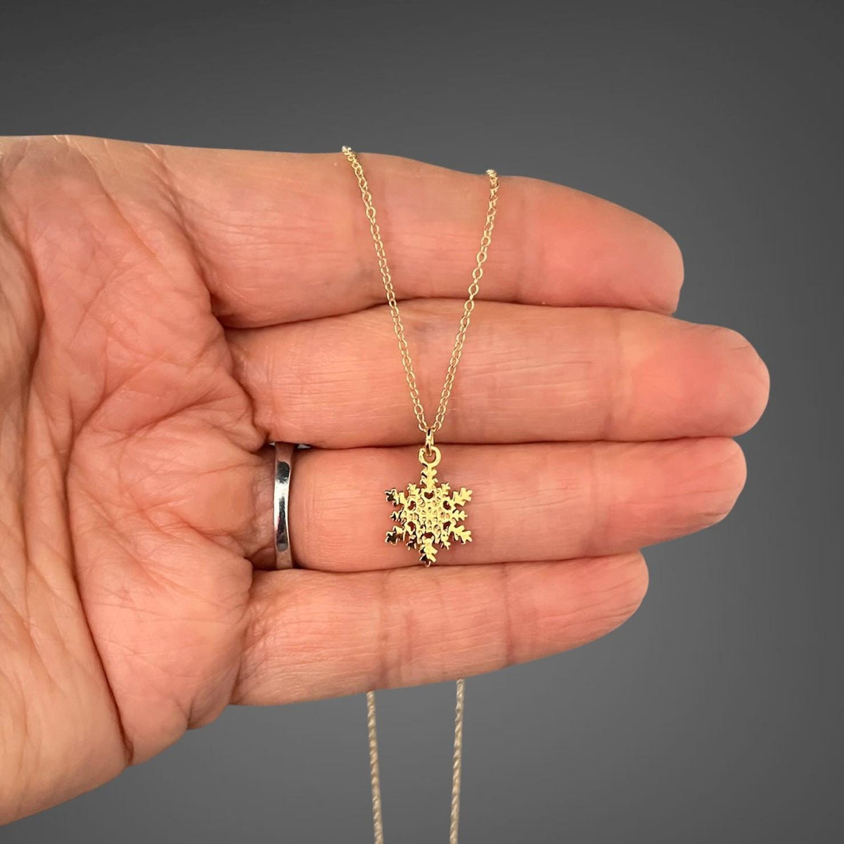 Gold snowflake charm necklace shown against a hand for scale
