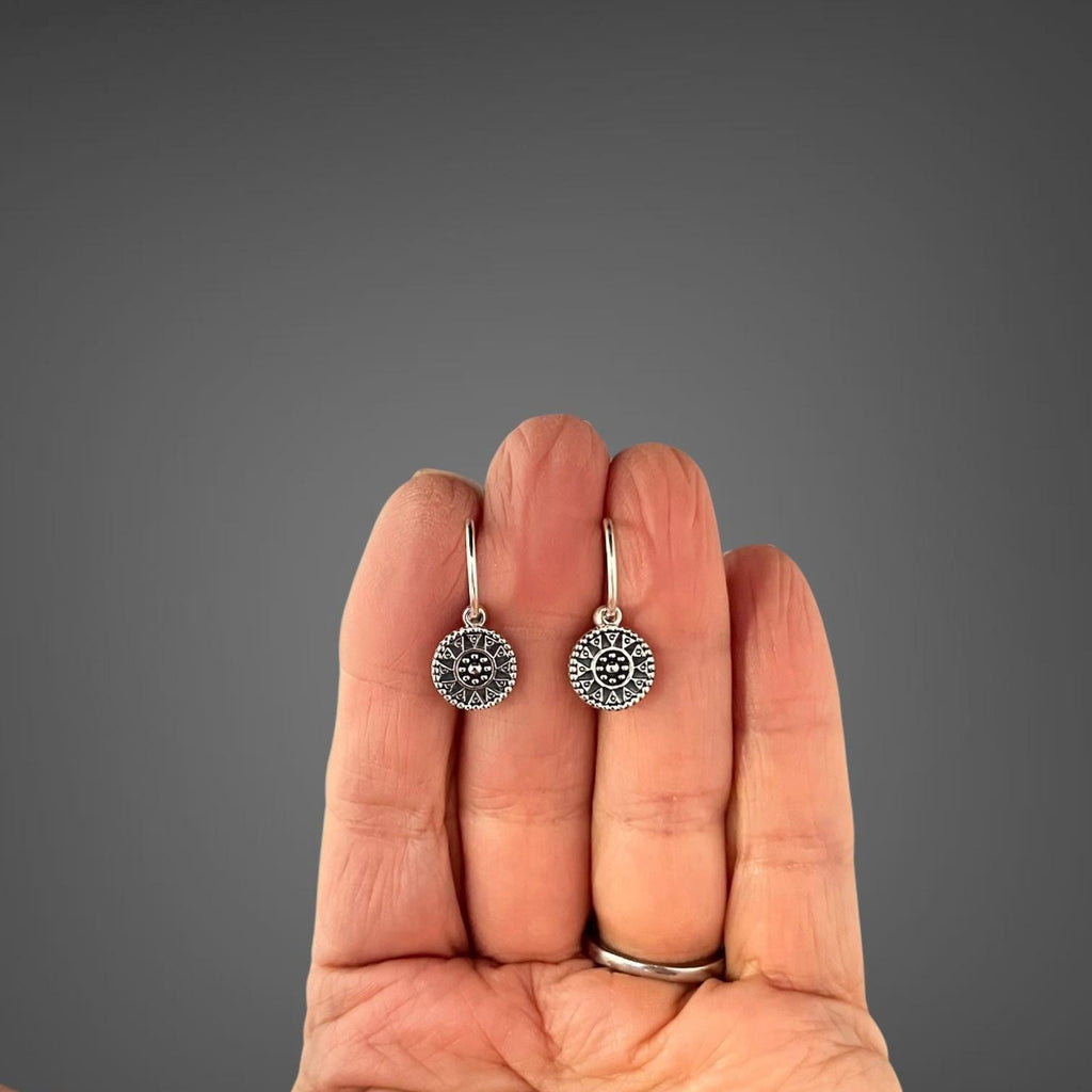 Sterling silver medallion charm earrings shown on a hand for scale
