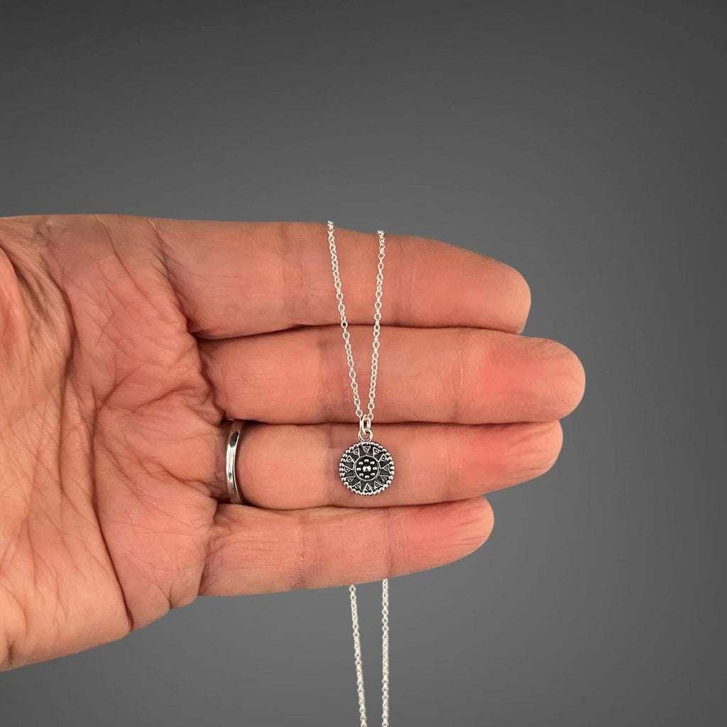 Sterling silver medallion necklace held across a hand to show pendant scale