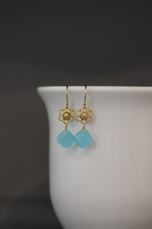 Gold earrings with turquoise beads on a white cup against a dark background