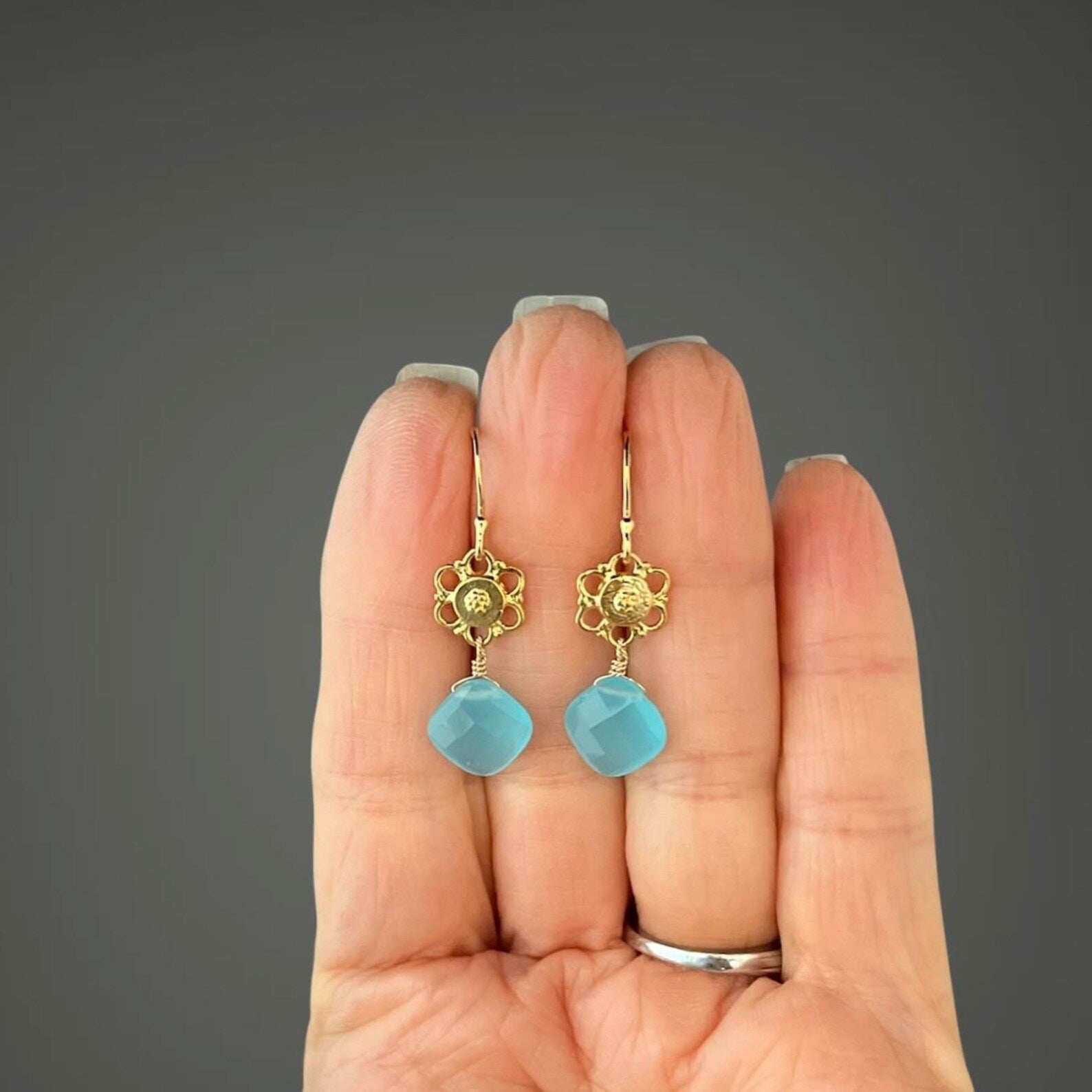 Gold earrings with blue stones held in a hand against a gray background