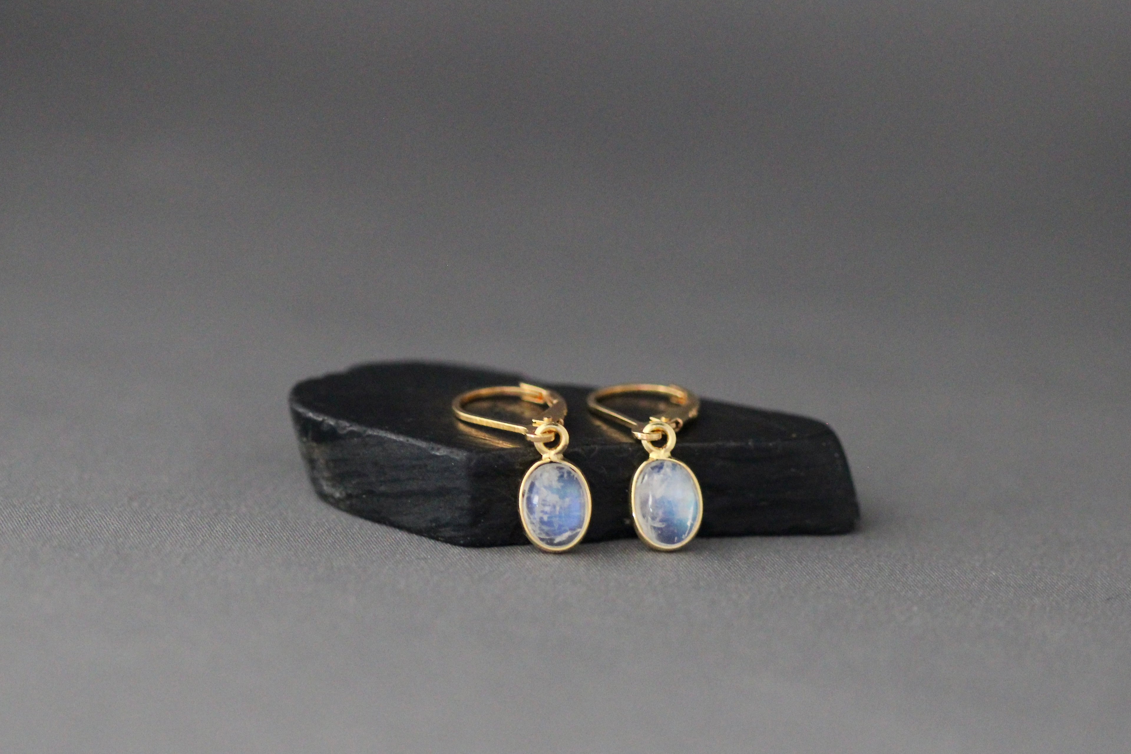 Gold leverback earrings featuring oval blue moonstone cabochon bezel drops