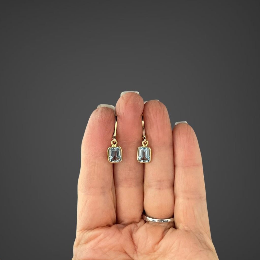 Gold vermeil leverback earrings with light blue emerald-cut bezel-set stones on hand
