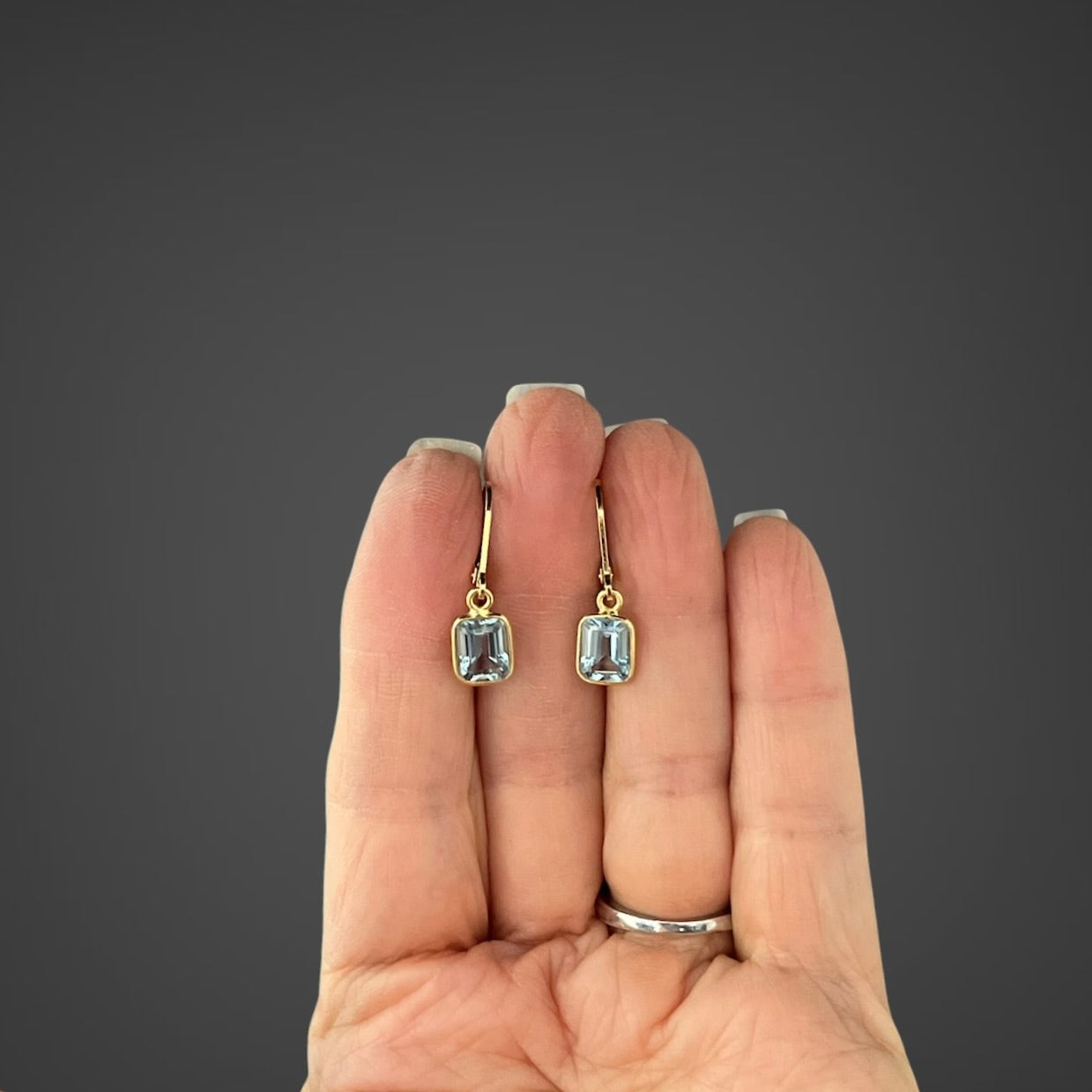 Gold vermeil leverback earrings with light blue emerald-cut bezel-set stones on hand