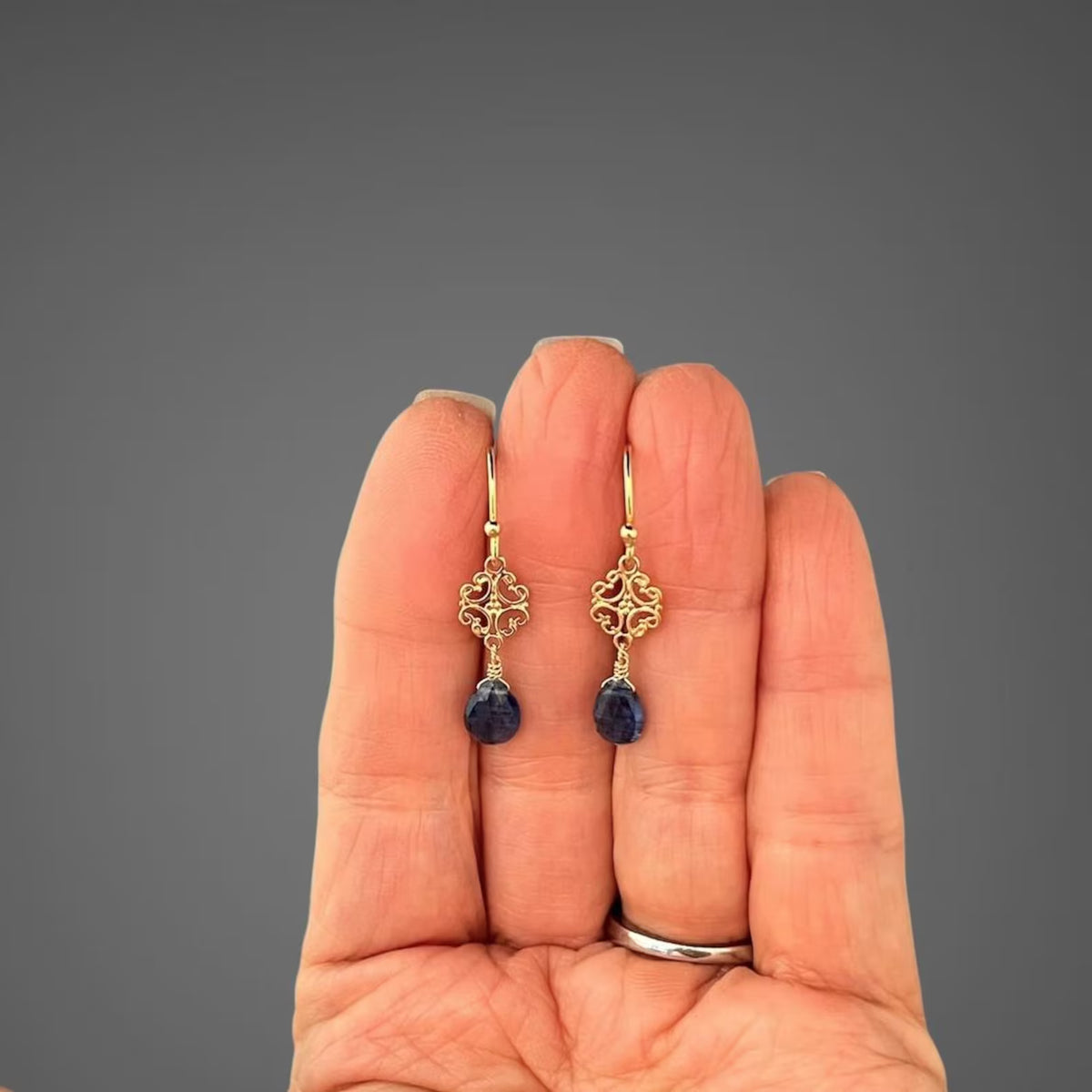 Blue kyanite teardrop earrings with filigree gold vermeil details, worn on hand