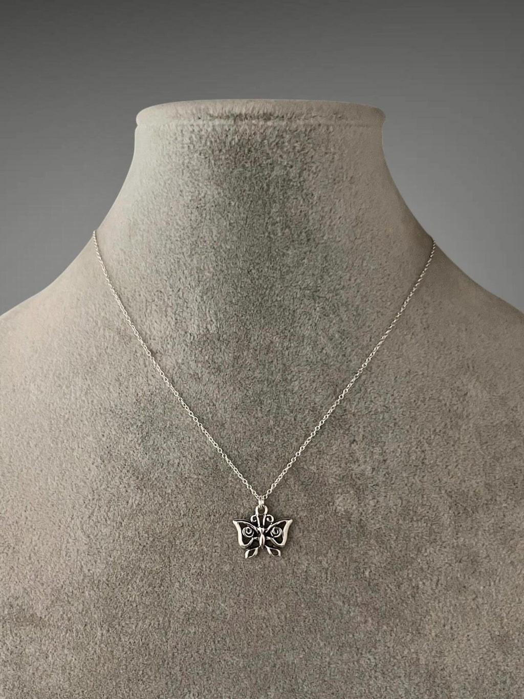 Sterling silver butterfly charm necklace on taupe fabric bust, pendant at center