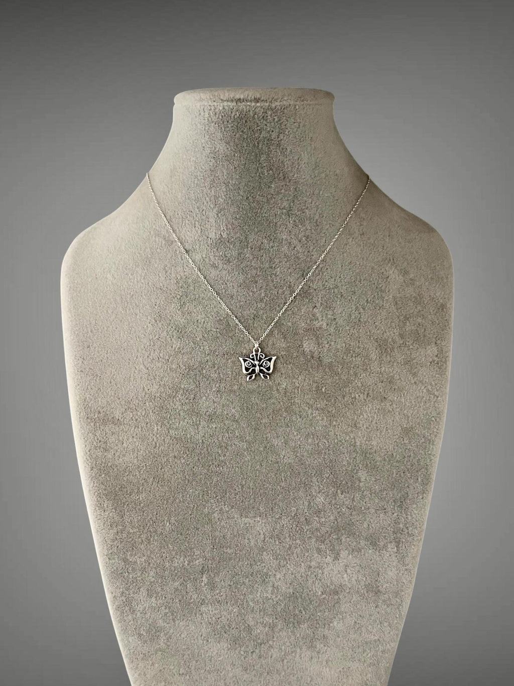 Sterling silver butterfly charm necklace on mannequin, small wing pendant at neckline
