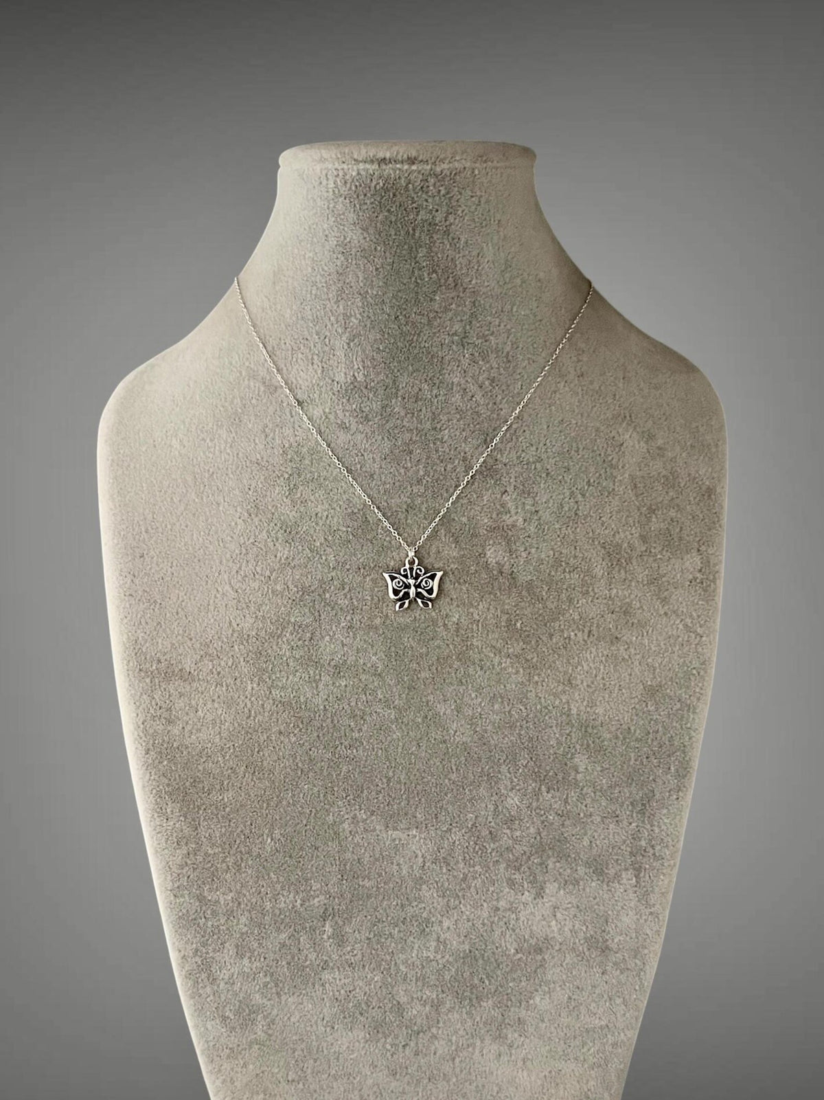 Sterling silver butterfly charm necklace on mannequin, small wing pendant at neckline