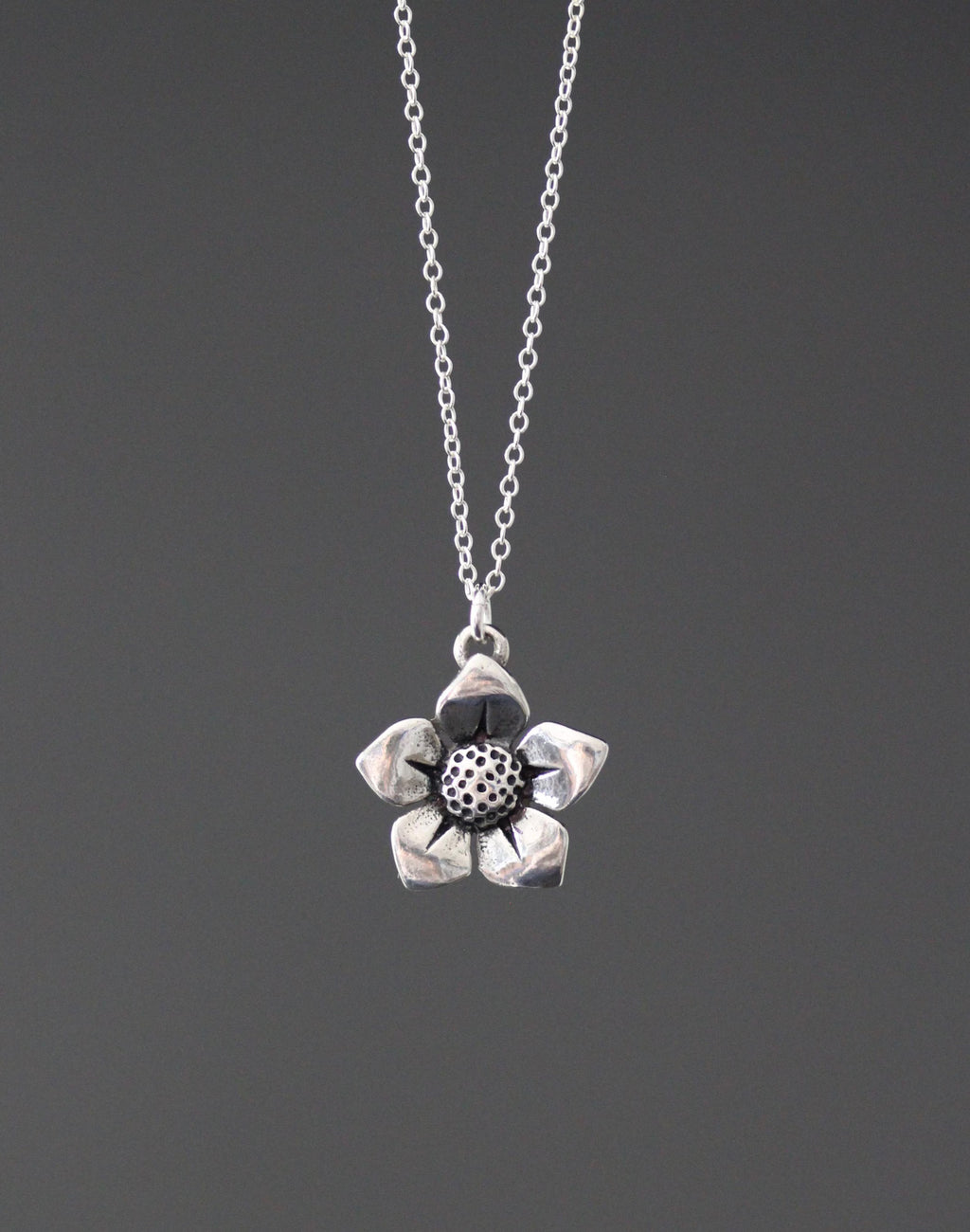 Sterling silver flower charm pendant necklace with round textured center, on fine chain.