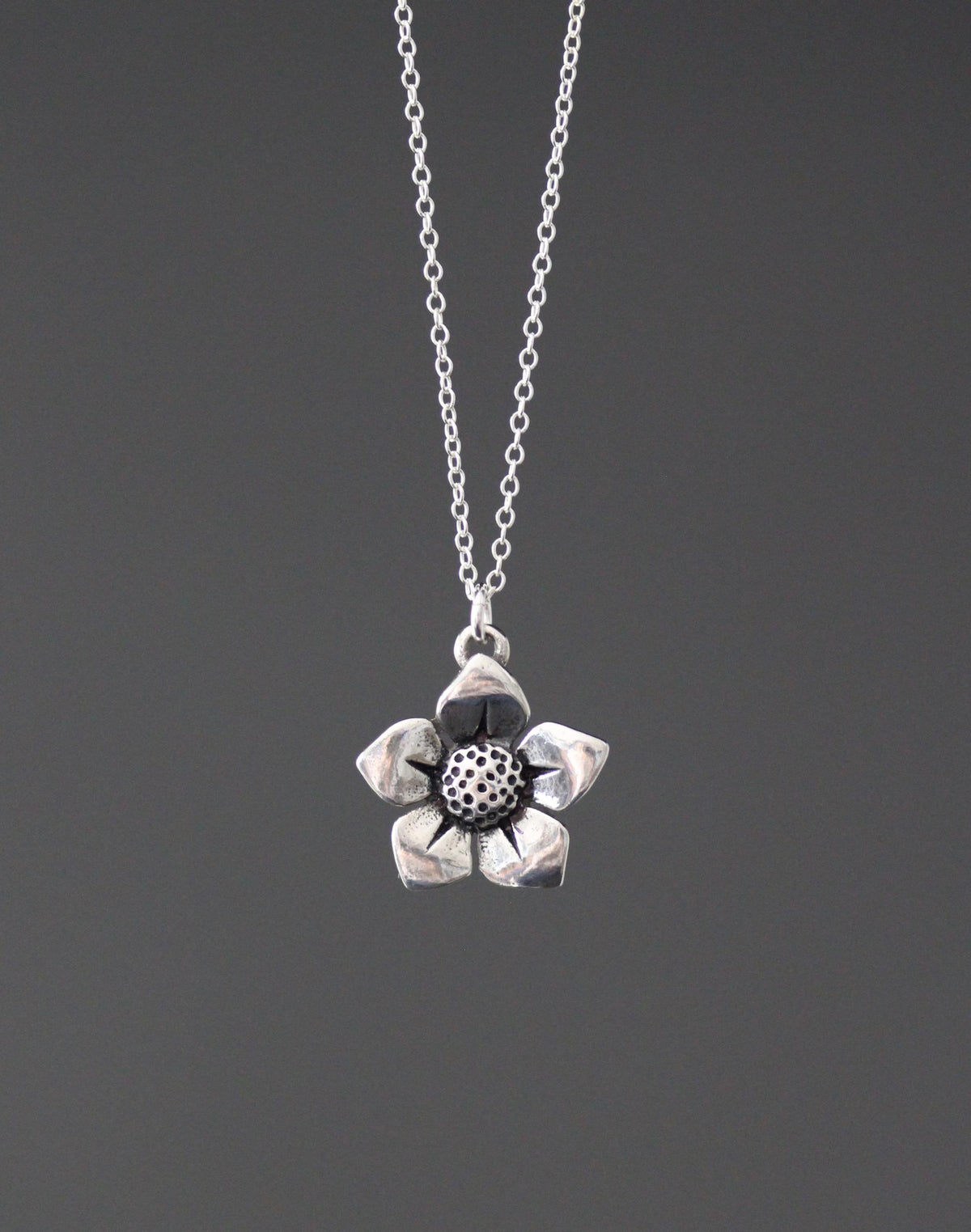 Sterling silver flower charm pendant necklace with round textured center, on fine chain.