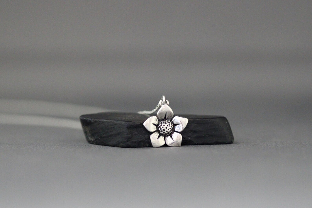 Sterling silver flower charm pendant with textured center, hanging on fine chain.
