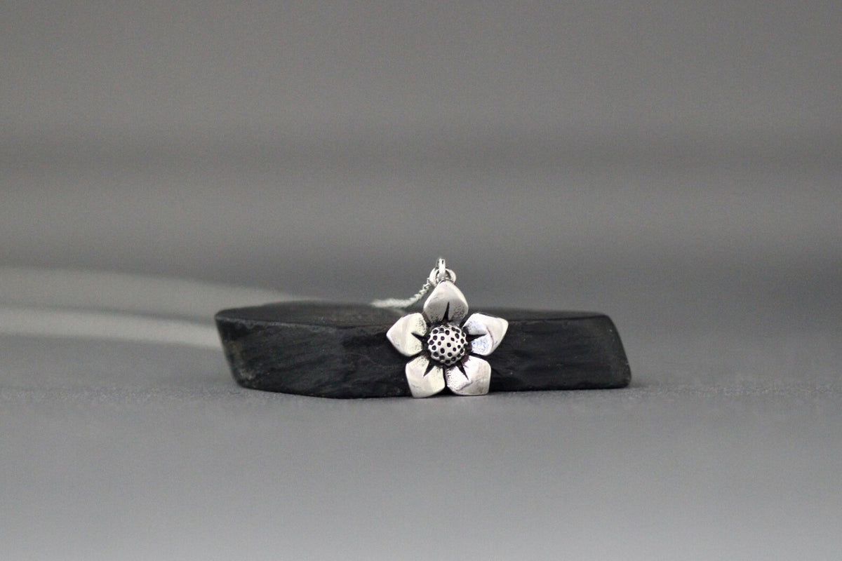 Sterling silver flower charm pendant with textured center, hanging on fine chain.