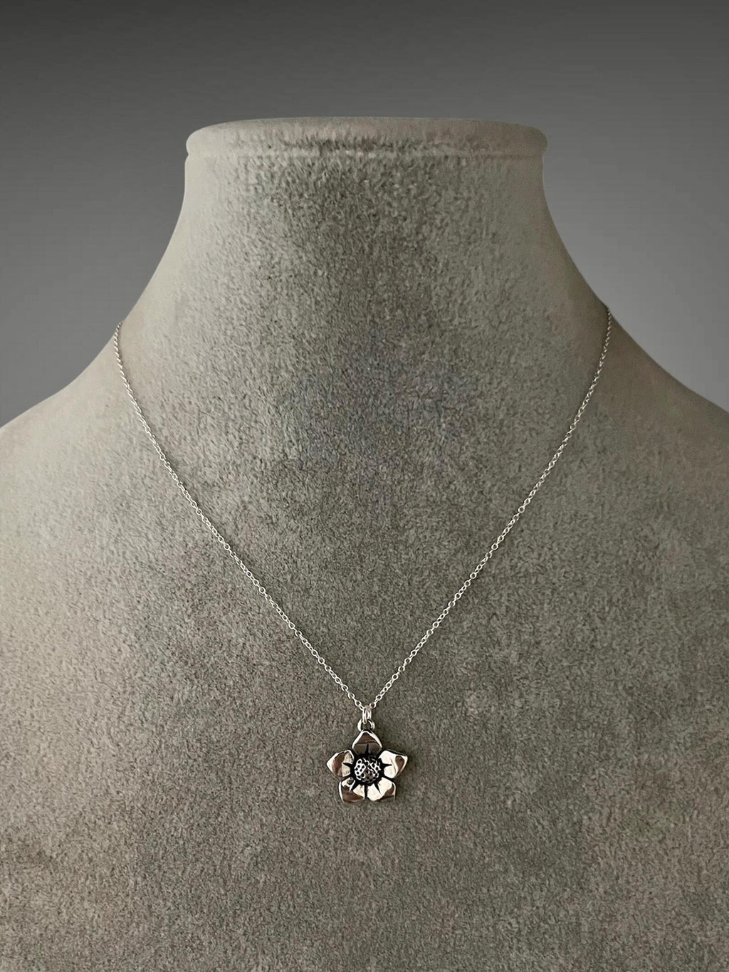 Sterling silver necklace with flower charm pendant on fine chain, close-up on bust display.