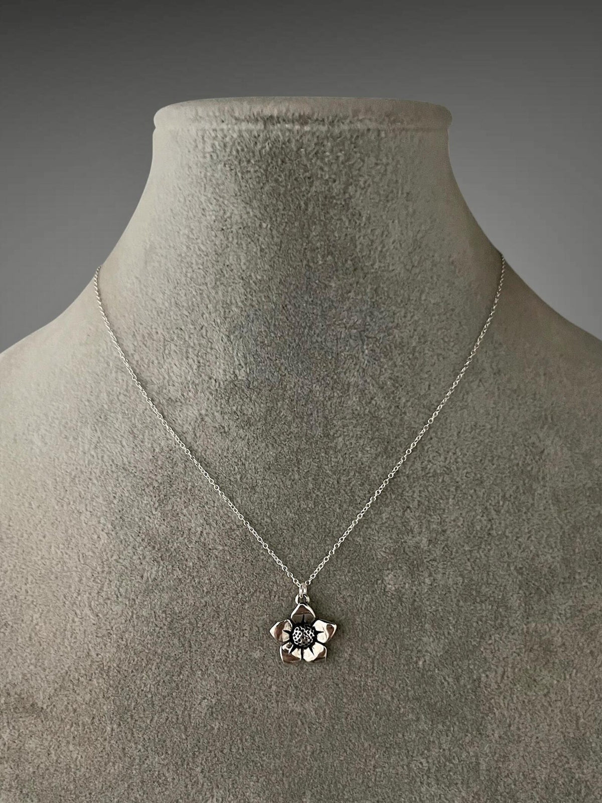 Sterling silver necklace with flower charm pendant on fine chain, close-up on bust display.