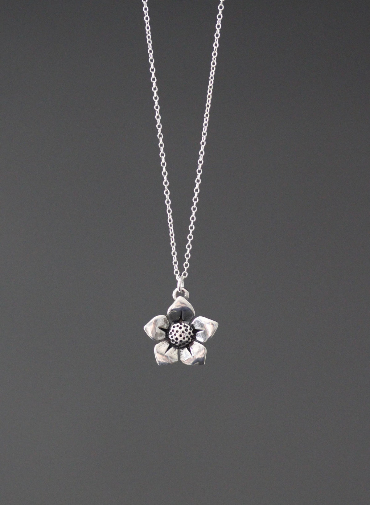 Sterling silver flower charm pendant on fine chain necklace, textured center flower design.