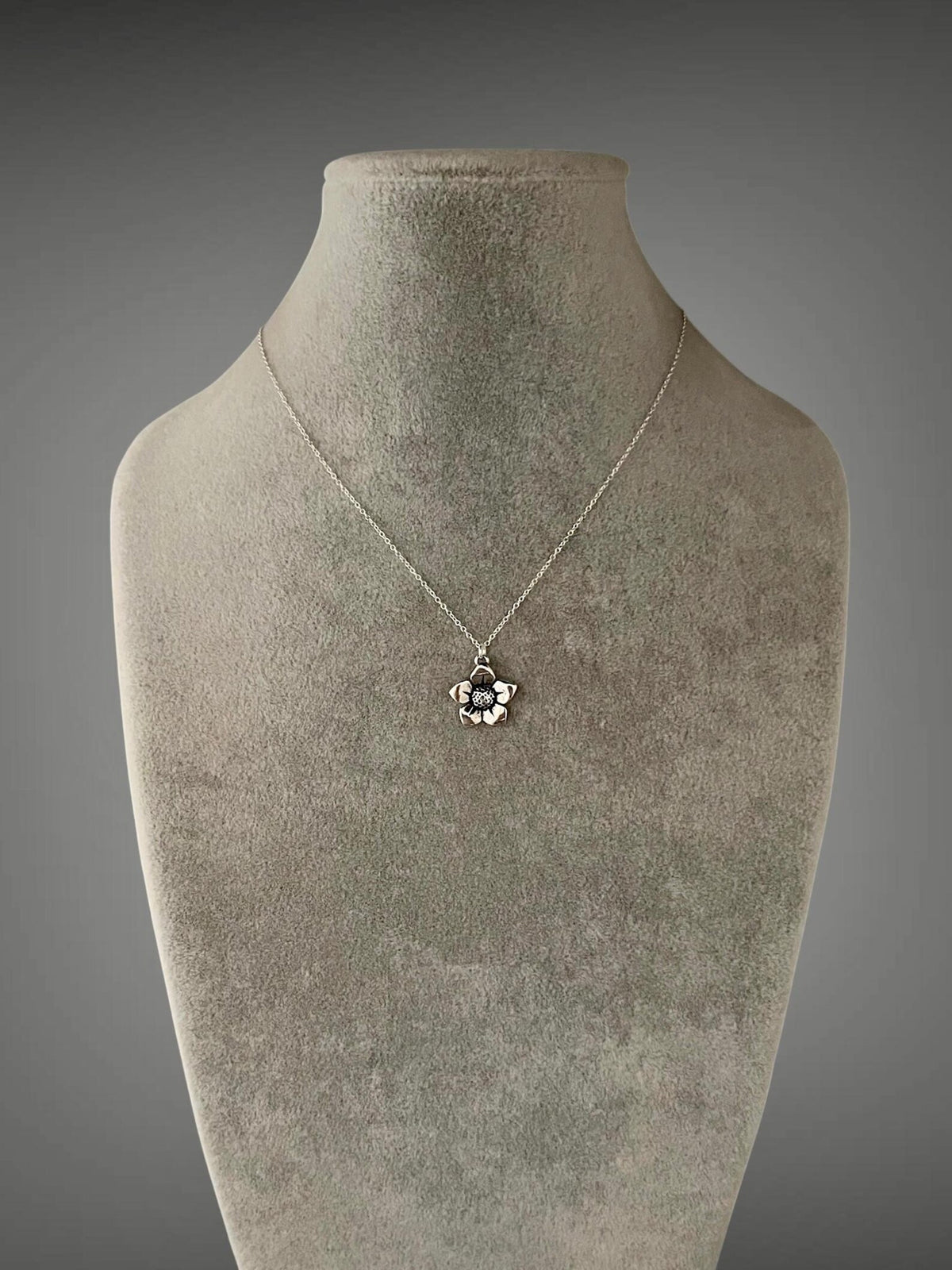 Sterling silver necklace with small flower charm on fine chain, detailed petal design.