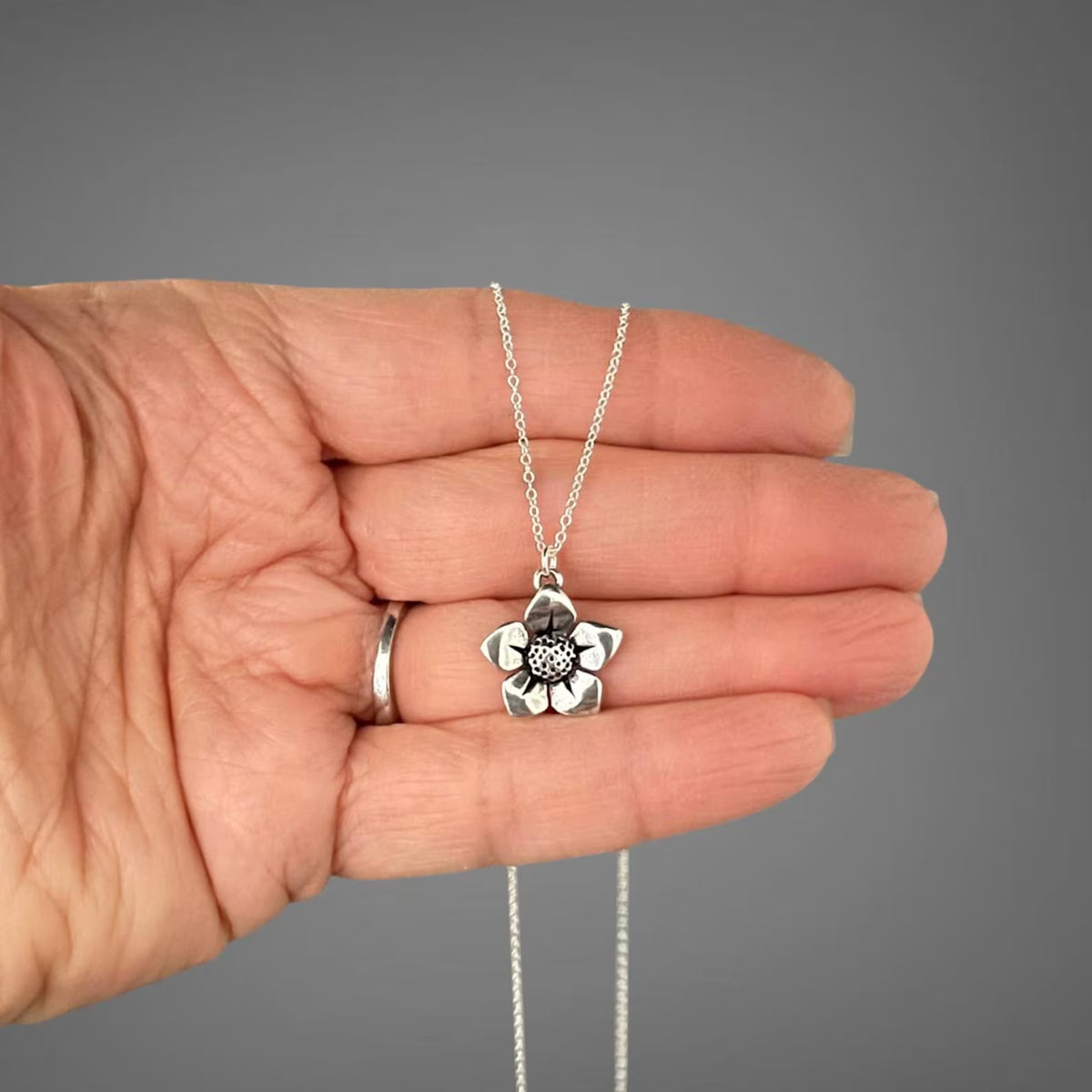 Sterling silver flower charm necklace held in hand, pendant with textured center on chain.