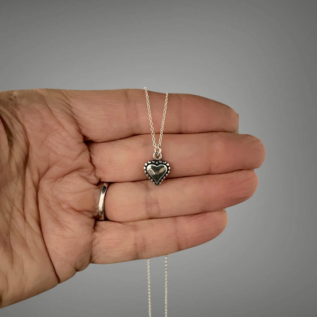 Sterling silver heart charm necklace held in hand on a thin chain