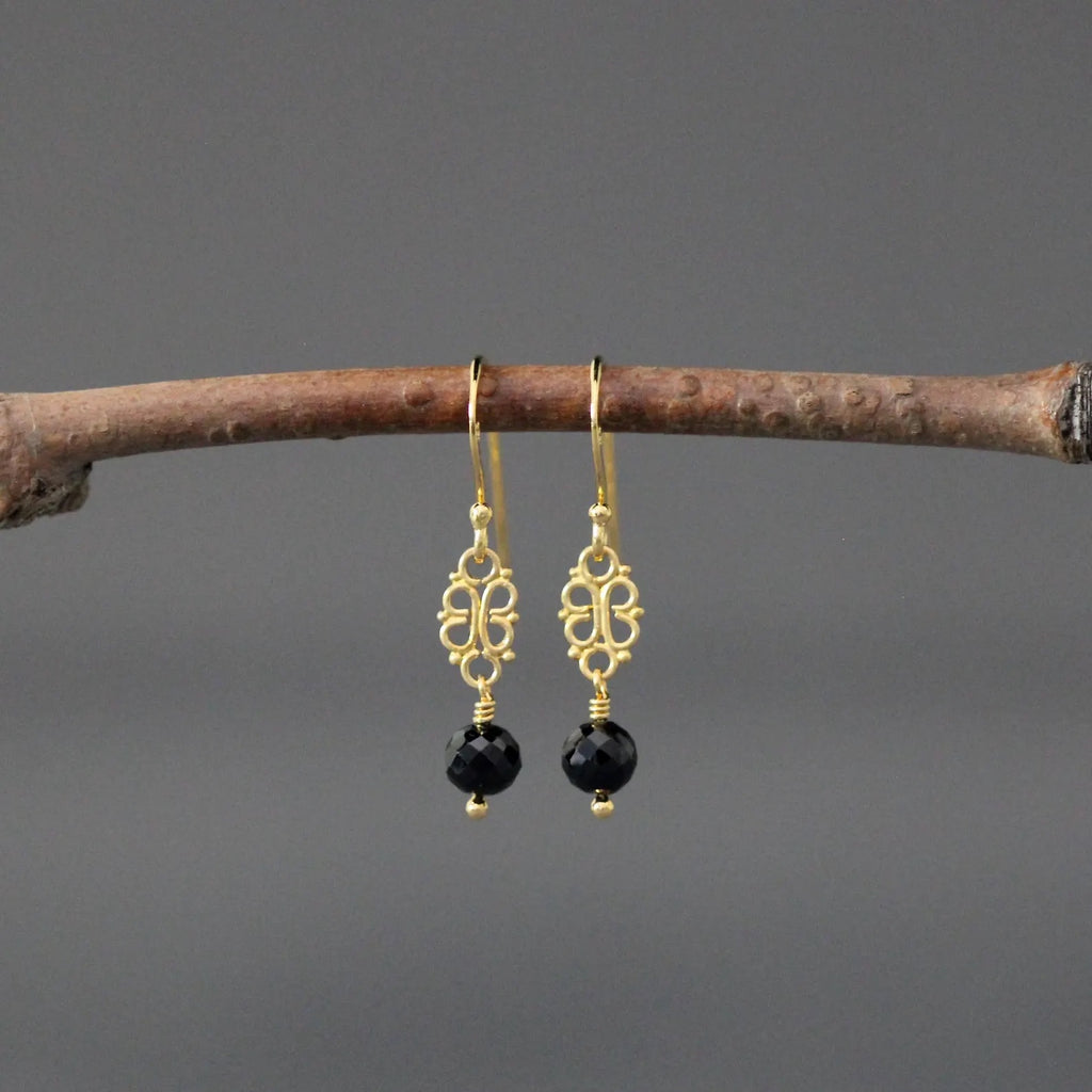 Gold earrings with black beads hanging on a branch against a gray background