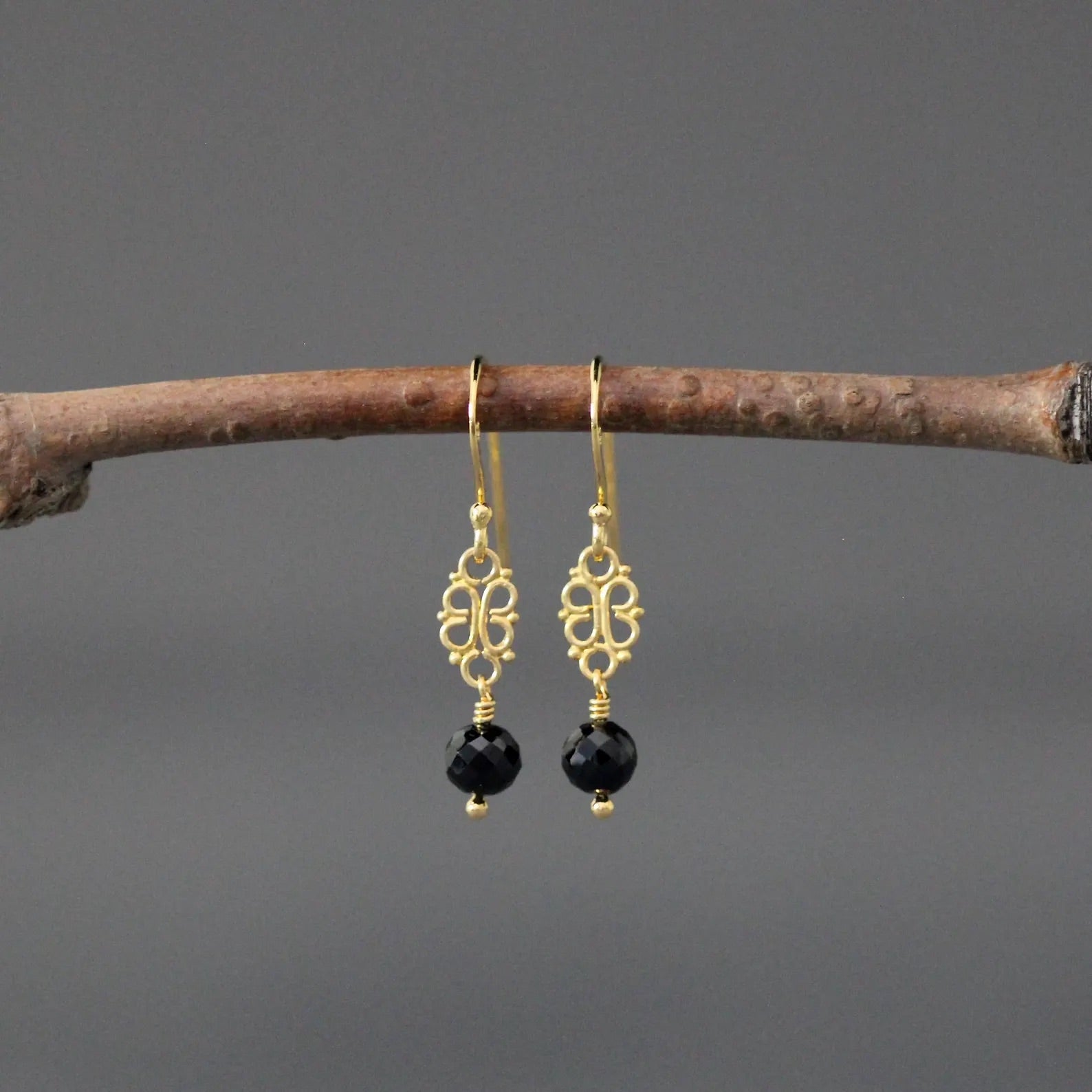 Gold earrings with black beads hanging on a branch against a gray background