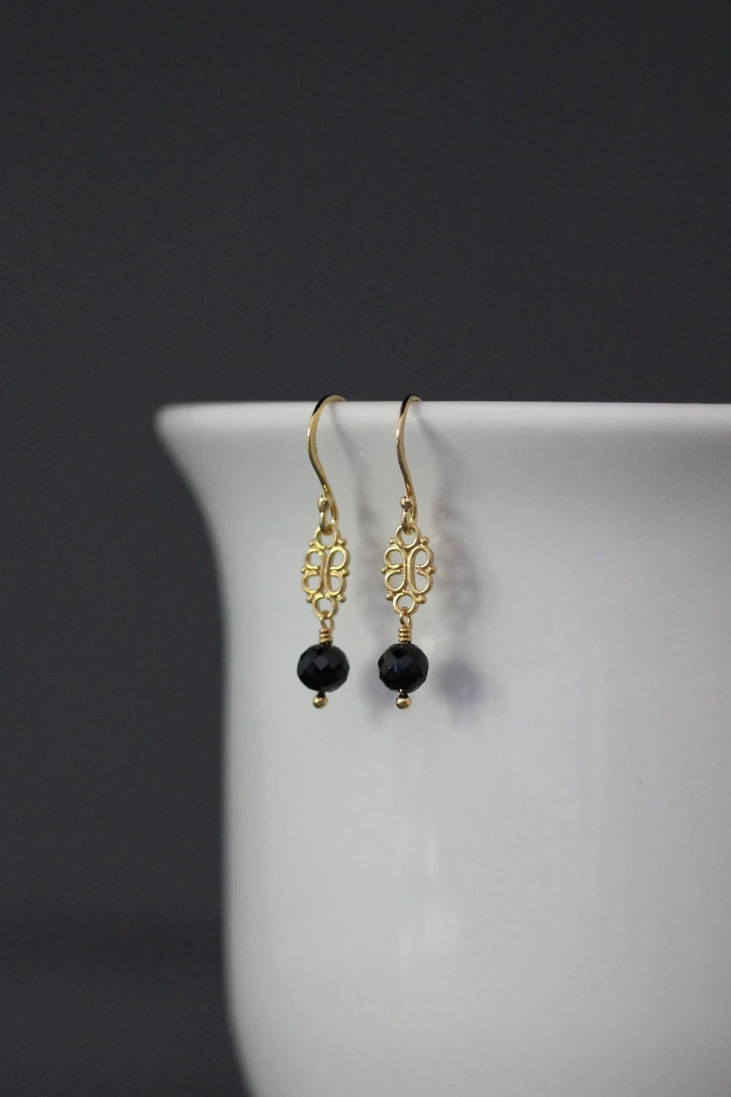 Gold earrings with black beads on a white surface against a dark background