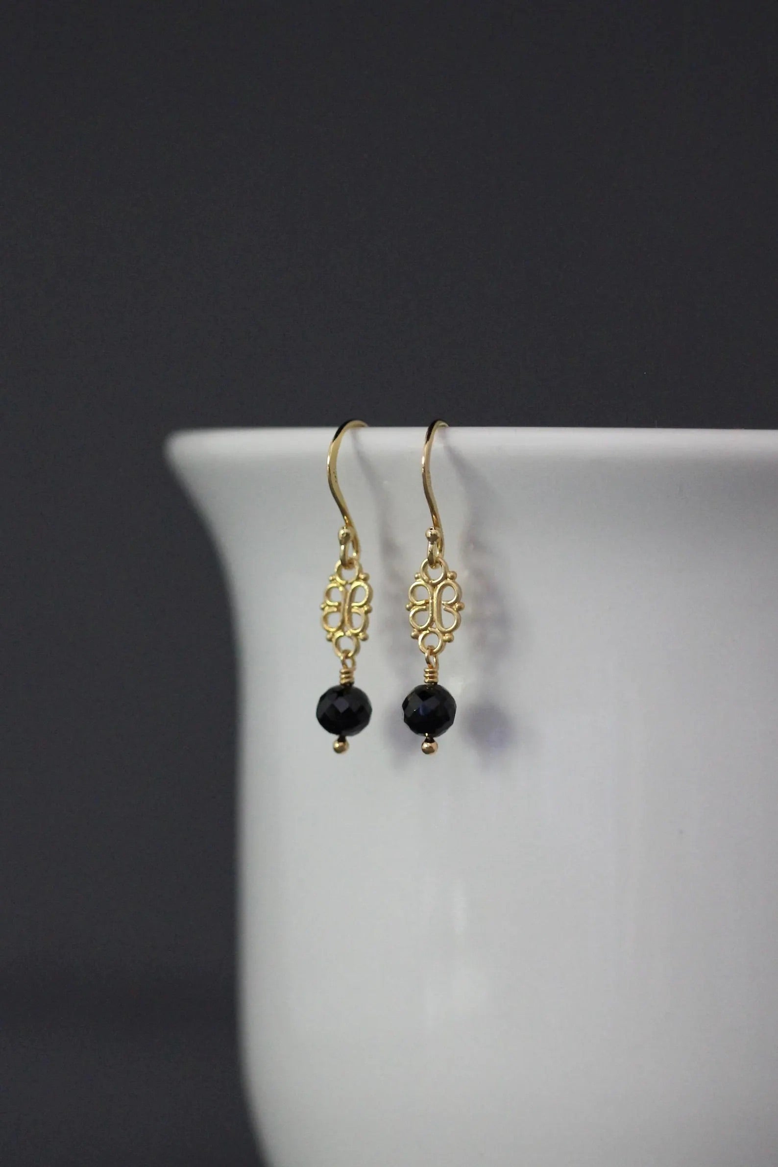 Gold earrings with black beads on a white surface against a dark background