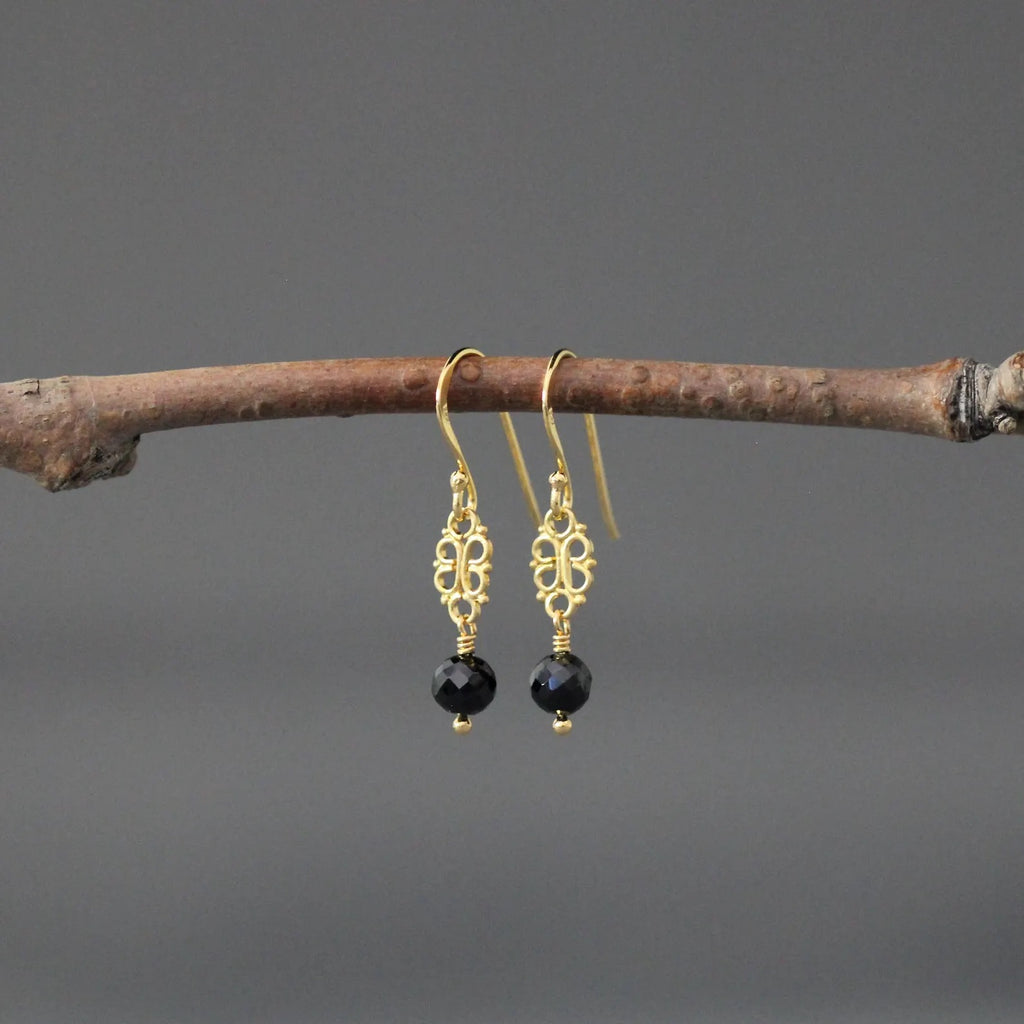 Gold earrings with black beads hanging on a branch against a gray background