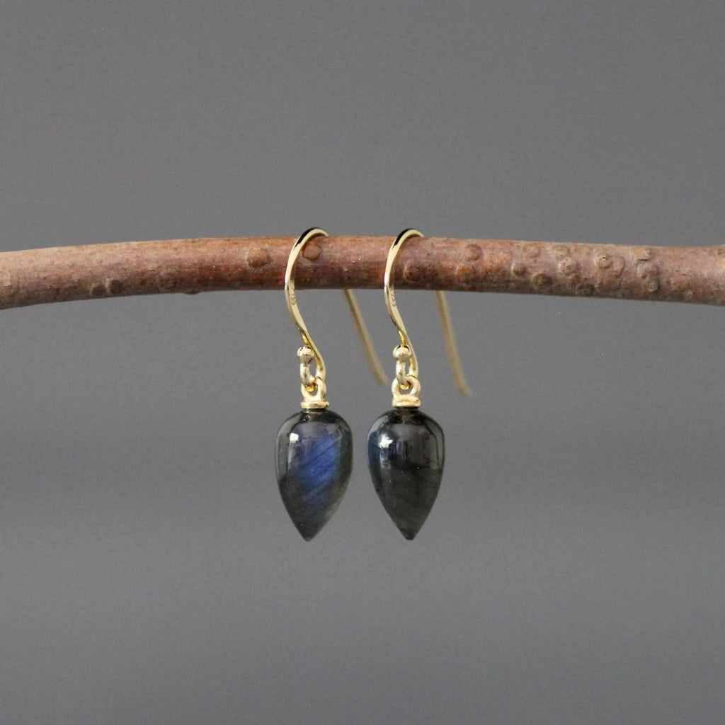 Gold earrings with black teardrop-shaped stones on a branch against a gray background