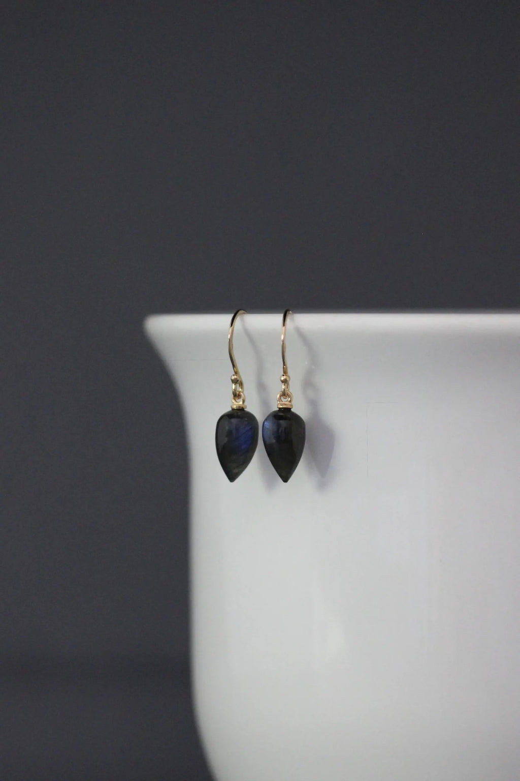 Pair of black teardrop earrings on a white stand with a dark background