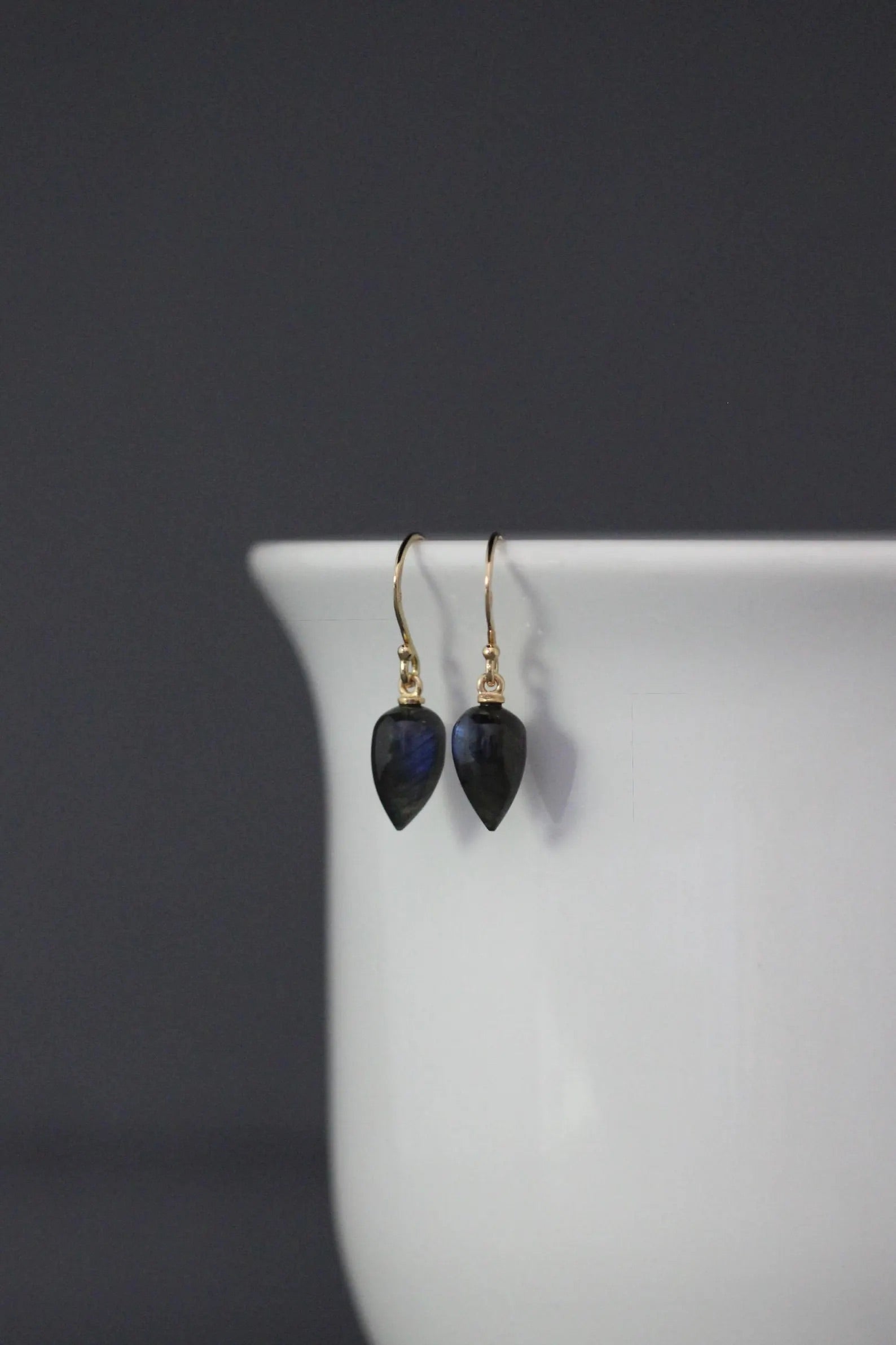 Pair of black teardrop earrings on a white stand with a dark background