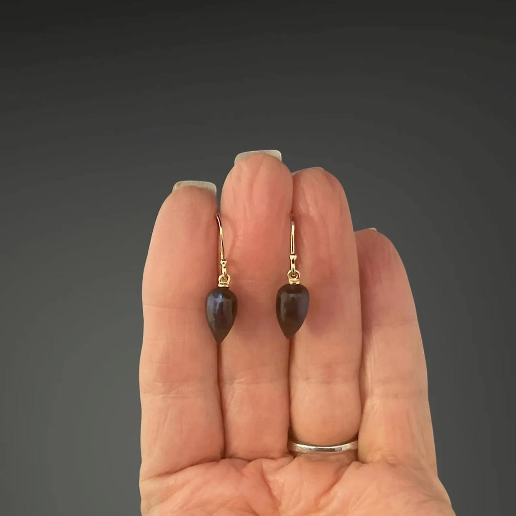 Heart-shaped earrings held between fingers against a dark background