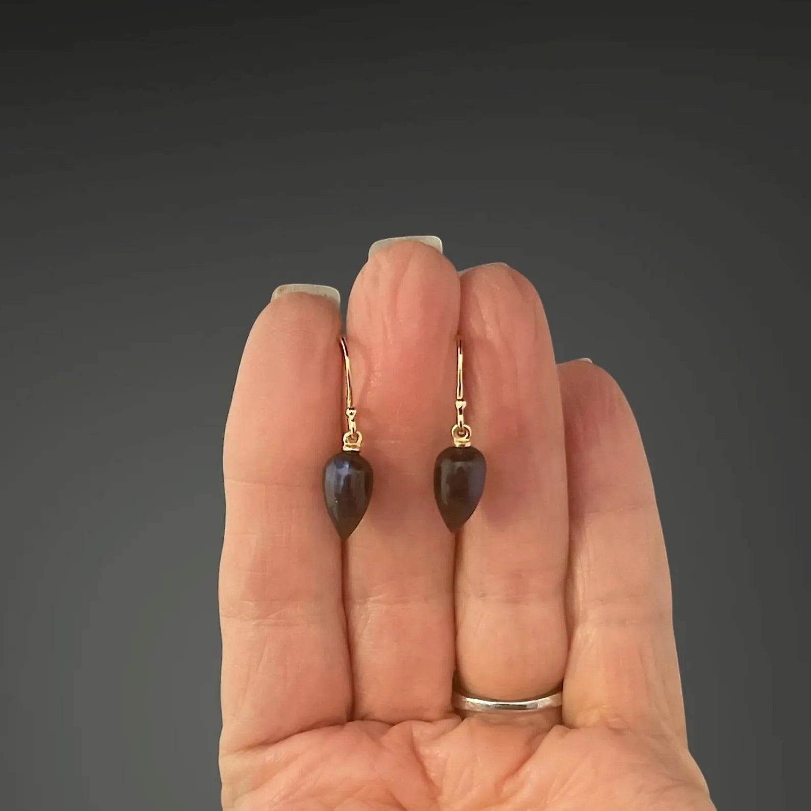Heart-shaped earrings held between fingers against a dark background