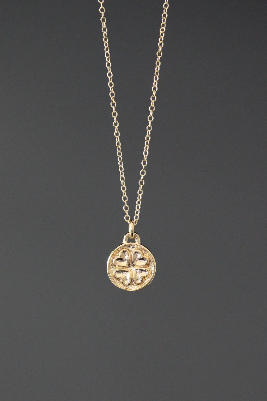 Gold necklace with a clover-shaped pendant on a dark gray background