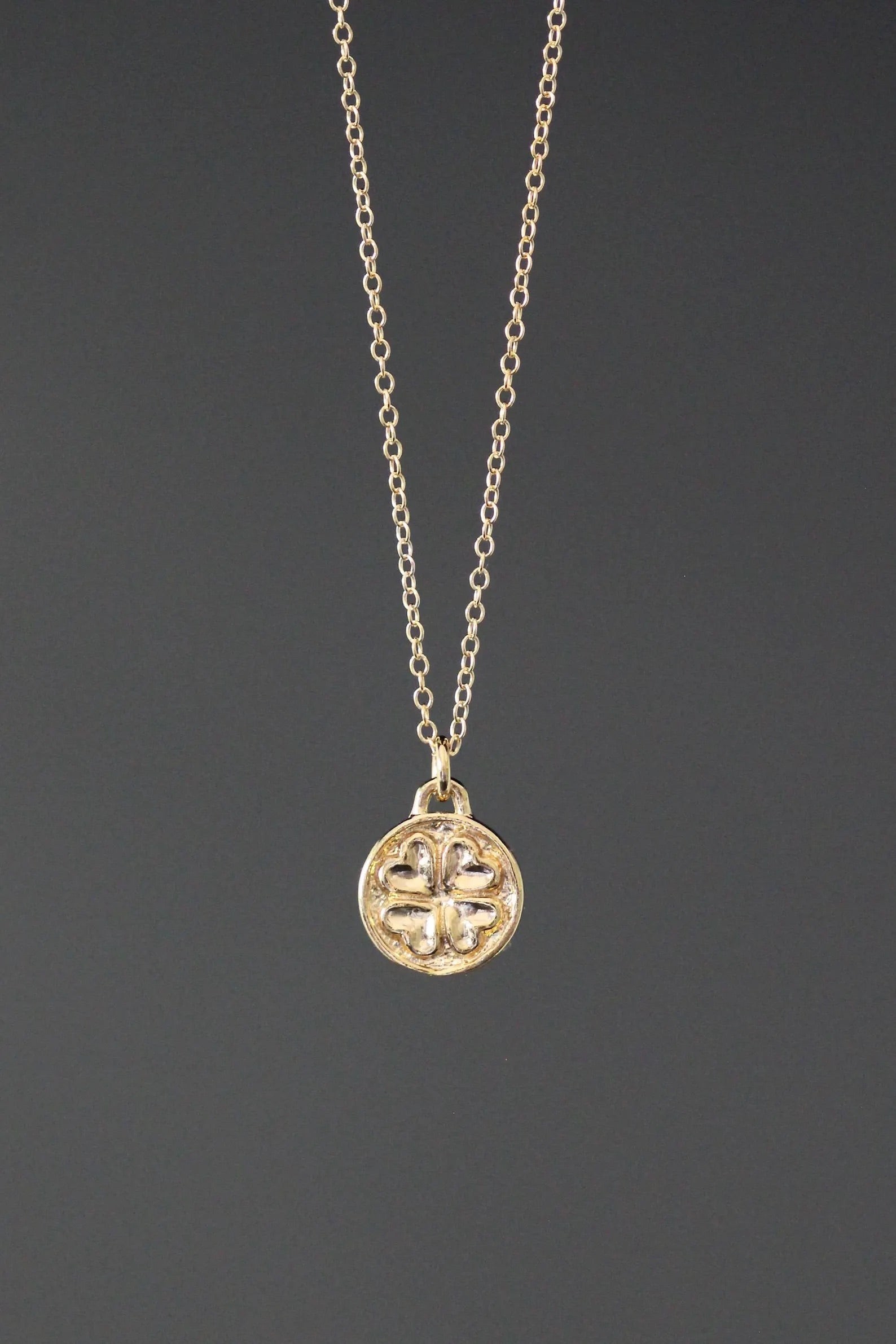 Gold necklace with a clover-shaped pendant on a dark gray background