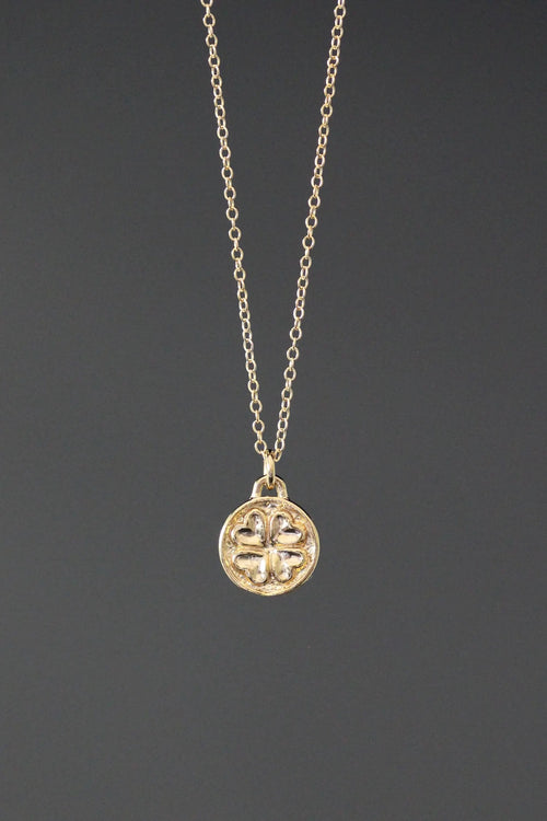 Gold necklace with a clover-shaped pendant on a dark gray background