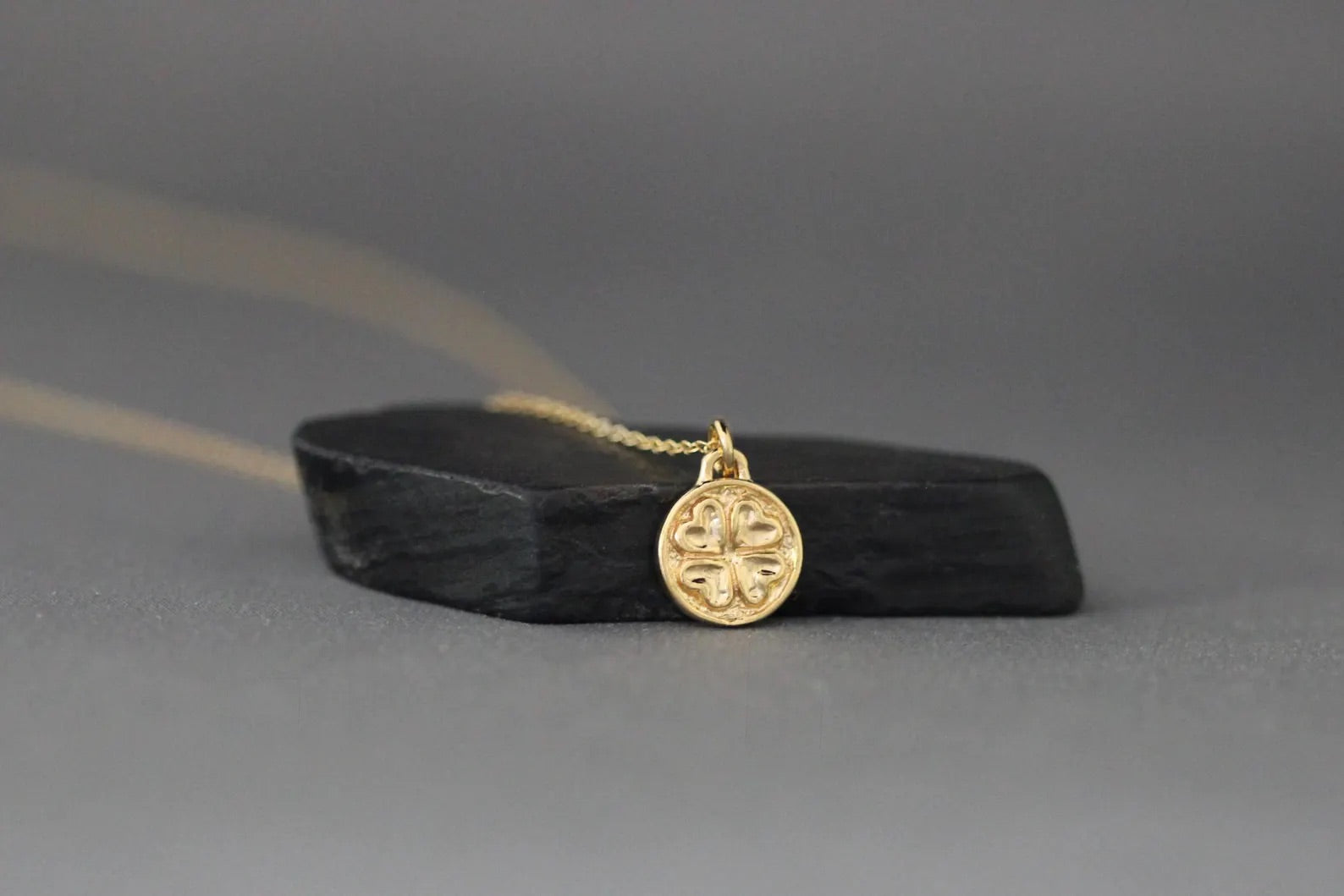Gold necklace with a circular pendant on a black stand against a gray background