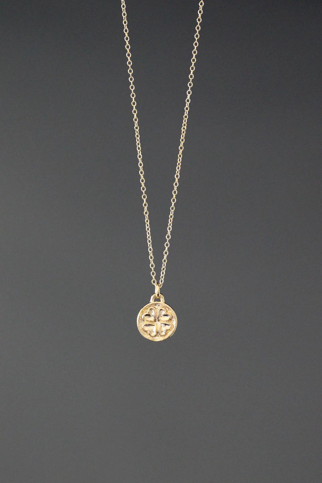 Gold necklace with a round pendant on a dark gray background