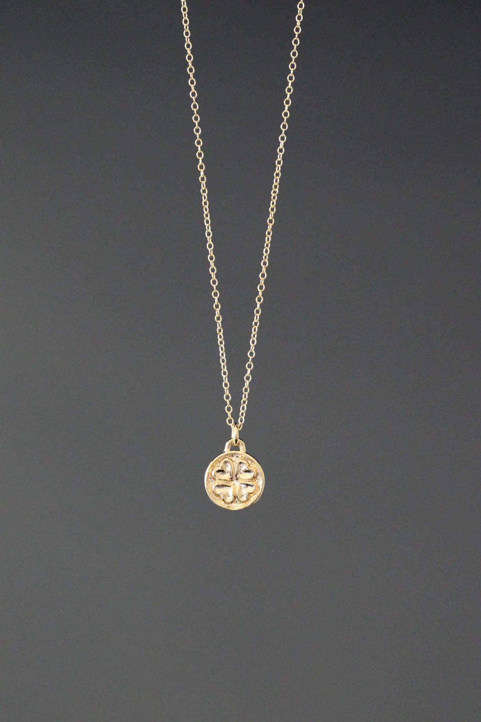 Gold necklace with a round pendant on a dark gray background